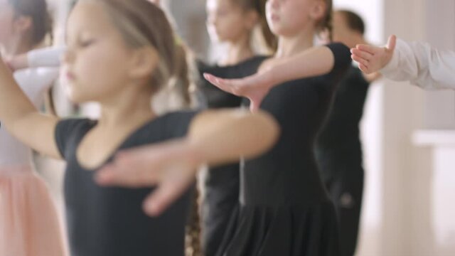 Group of confident serious boys and girls making steps in fourth ballet position in dance studio. Concentrated Caucasian children rehearsing in dancing school indoors. Art and talent concept.