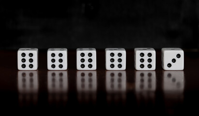 Six dice on a table with reflection and black background, five dice showing six, one dice showing three