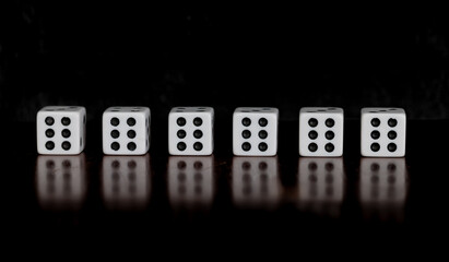 Six dice, all showing six, on a table with reflection and black background