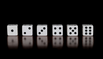 Six dice showing one through six on a table with reflection and black background