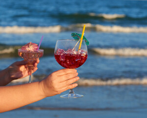 A cocktail with ice perched on the sand of the beach