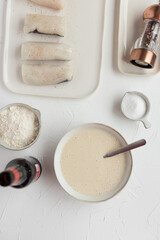 Overhead view of tempura ingredients next to a final tempura butter ready to fry hake loins.