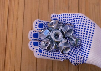 Metal shine nuts in the hand of the worker with protective gloves - Wooden background