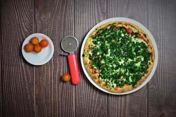 Spinach pizza with mozzarella and tomato on rustic wooden table
