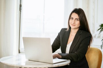 The psychologist is a brunette of Caucasian appearance. Sitting in a comfortable chair and reading an electronic textbook on a laptop. The student studies the basics of economics. College education.