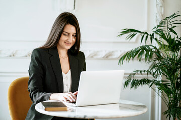 A brunette psychologist in a business suit. Sitting in a comfortable chair and reading an electronic textbook on a laptop. The student studies the basics of economics. Online training in a cafe.