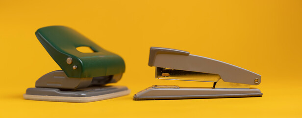 Office tools with a stapler and perforator still life against a seamless solid yellow background
