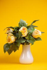 Vertical frame of yellow roses in green foliage in small white vase against a smooth monochrome background