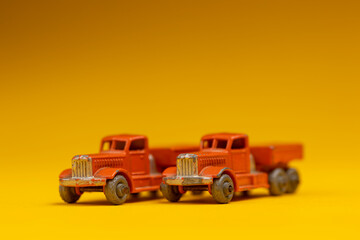 Fototapeta na wymiar Two identical miniature orange old timer industrial vintage cars next to each other. Studio toy still life against a seamless yellow background.