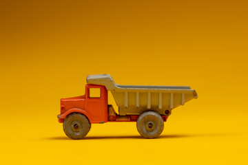 Isolated industrial miniature truck with open container and sharp shadow underneath. Studio still life old fashion toy against a seamless yellow background.