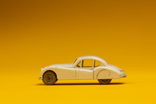 White miniature vintage type car with sharp shadow underneath. Studio still life old fashion toy against a seamless yellow background.