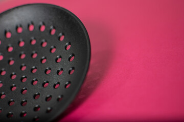 Black Plastic holed skimmer  cooking spatula on pink background with space to copy
