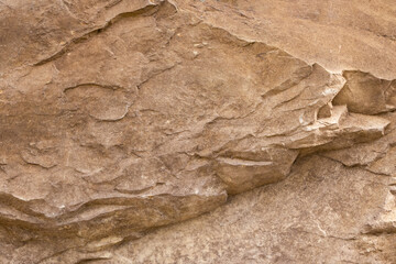 An abstract macro shot of a textured stone wall in light brown earth tones.