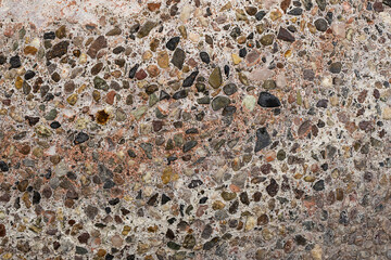 An abstract shot of a boulder with many colorful rocks imbedded in it.