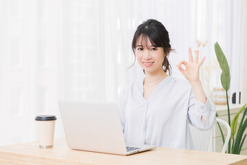 部屋でノートパソコンを使いながらOKのジェスチャーをする若い女性