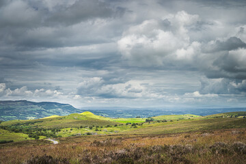 Green hills with pastures illuminated by patches of sunlight and stormy sky in background, Cuilcagh Mountain Park, Northern Ireland