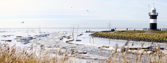 Leuchtturm in Wremen im Winter mit Schnee und Eisschollen auf dem Weltnaturerbe Wattenmeer in...