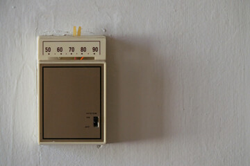 An old, analog temperature control thermostat is shown on a wall up close, with text or copy space...