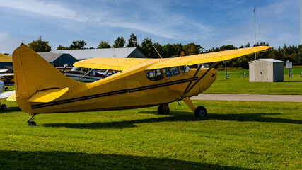 Fototapeta na wymiar Yellow private airplane next to hangars and a runway in the summer