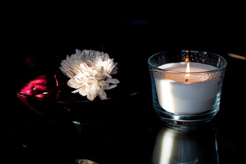 Bright white flower decoration next to white scented candle flame with dark background.