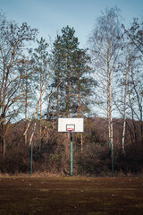 Empty old basketball court with a new basketball hoop with trees in the background