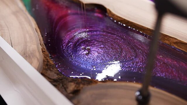 Process making of a craft resin and wood table. Liquid epoxy is poured into a mold with wooden blanks.