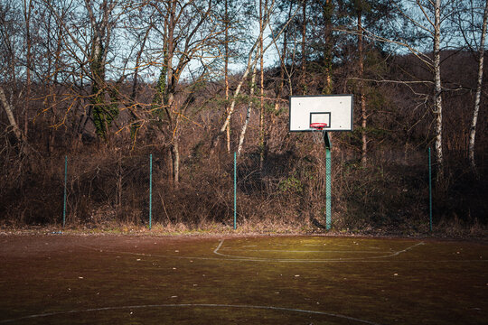 Empty old basketball court with a new basketball hoop with trees in the background