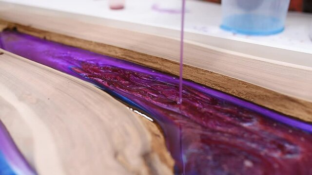Process making of a craft resin and wood table. Liquid epoxy is poured into a mold with wooden blanks.