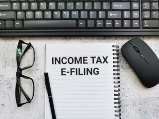 Selective focus phrase INCOME TAX E Filing written on note book with pen, eye glasses, wireless...