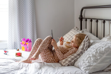 Little girl using a digital tablet while laying on a bed at home