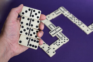 Male hand holding Old fashioned dirty domino with a solid prurple backround
