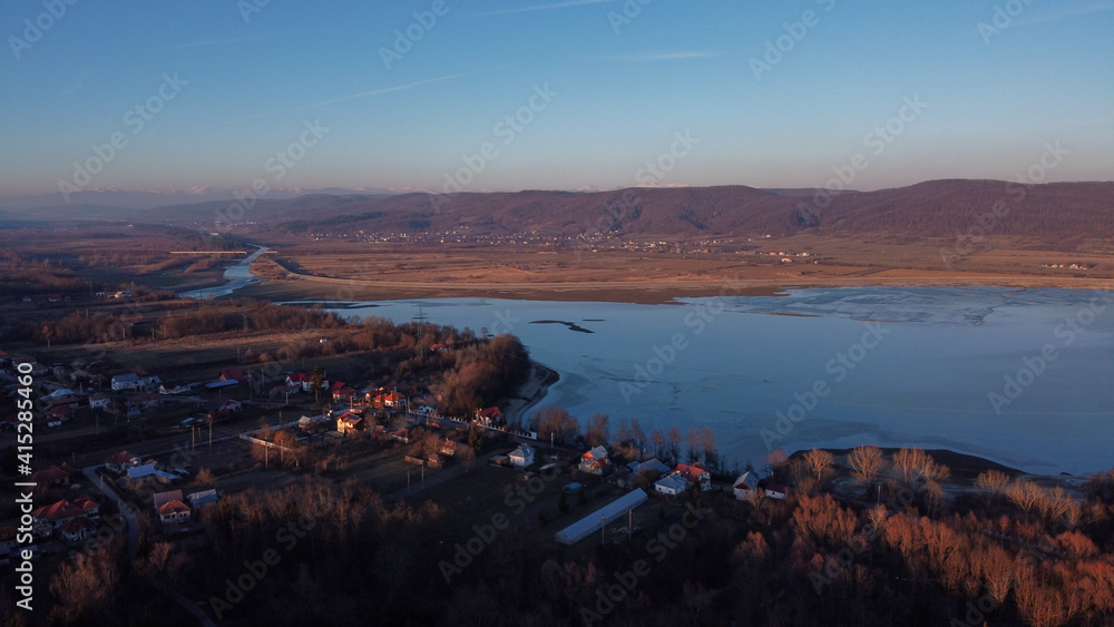 Sticker Aerial shot of a beautiful lake with buildings and trees in the background of mountains at sunset