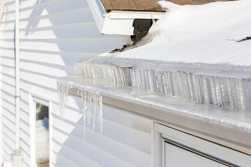 Roof gutter full of ice and icicles after winter storm. Concept of roof damage, home maintenance and repair.