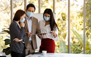 coronavirus prevention in the office. Group of Asian business people wearing face masks standing reading working discussion in a meeting room. Covid-19 new normal lifestyle concept