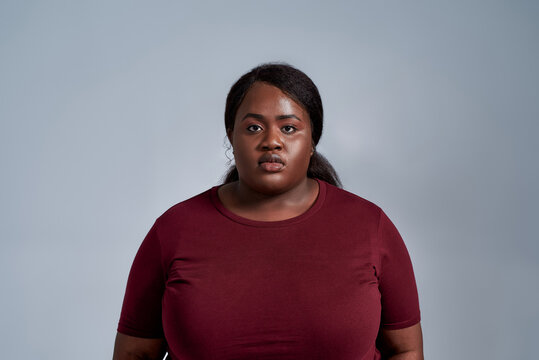 Portrait of serious plus size young african american woman in casual clothes standing isolated over gray background