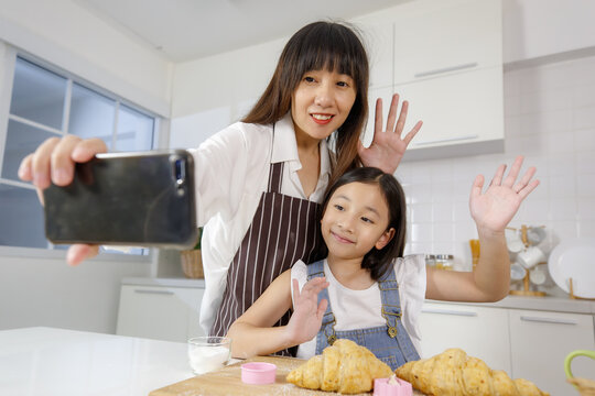 A cute and beautiful mother with young and little daughter, 7 years old, taking a selfie photo with a smartphone in modern kitchen. Concept love and relationship of family.