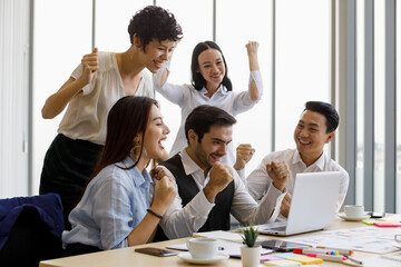 Group of five diversity businessmen, two men and three women, looking at notebook computer screen and rise hands with excited and happy.