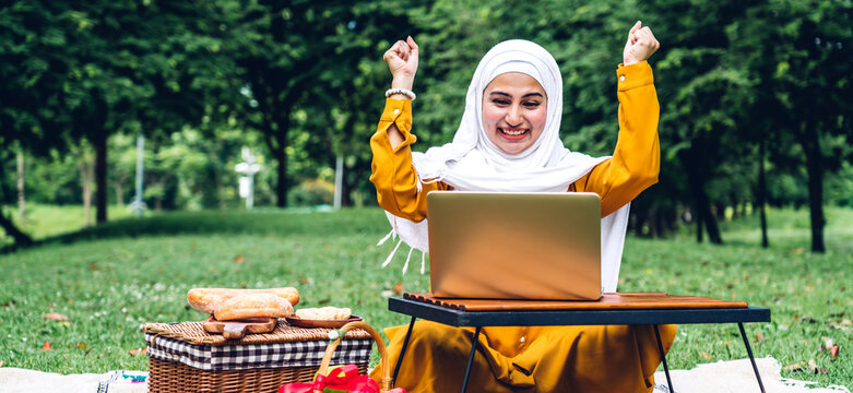 Portrait of happy arabic muslim woman with hijab dress smiling and using laptop cumputer in summer park