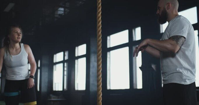 Beautiful young sporty blonde woman practice rope climbing with professional male coach at modern cross fit gym workout