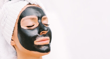 Beautiful young woman with black purifying charcoal facial mask. Cosmetic procedures, mask for skin care in spa salon. Copy space