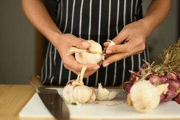 hands of a person with red onion and garlic picking on white board in the kitchen