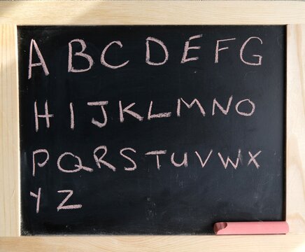alphabet written on black chalkboard with pink chalk.