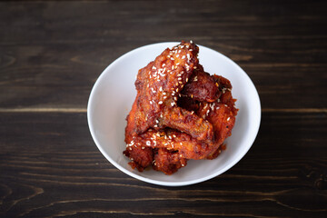 Chunks of fried chicken in a spicy sauce and sesame seeds. Food Korean cuisine on a wooden background.