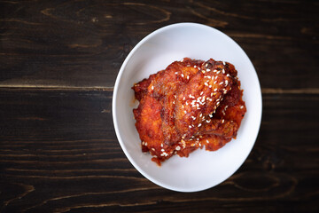 Chunks of fried chicken in a spicy sauce and sesame seeds. Food Korean cuisine on a wooden background.