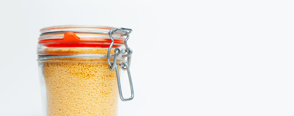 Close-up of raw couscous in glass jar on white background with copy space.