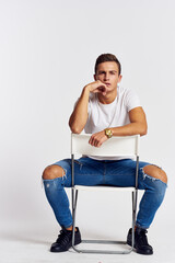 A man in jeans sits on a chair backwards and and ripped jeans T-shirt front view