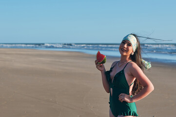 Woman in one-piece swimsuit holding a slice of watermelon on the beach