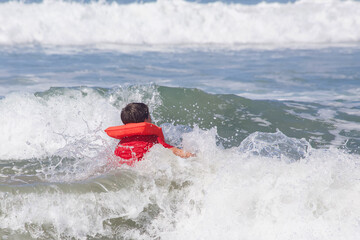 A young boy wearing an orange life vest is floating in the ocean and is surrounded by waves.