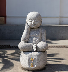 Stone figurine of sitting little monk thinking and meditating in courtyard of Qibao Temple, a Buddhist monastery in Qibao Old Town, Minhang, Shanghai, China.