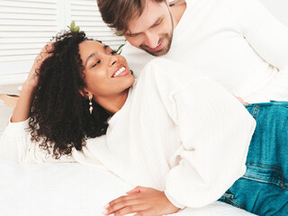 Smiling beautiful woman and her handsome boyfriend. Happy cheerful multiracial family having tender moments. Multiethnic models lying in bed and hugging in white interior. Embracing each other